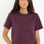 Woman wearing a purple t-shirt and blue jeans against a white background