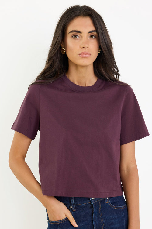 Woman wearing a purple t-shirt and blue jeans against a white background