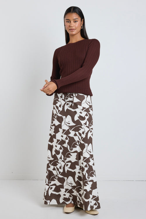 Model wears brown pattern maxi skirt with a tie waist and a long sleeve brown top. 