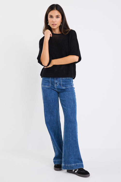 our model wears a black crochet knit top with mid blue jeans