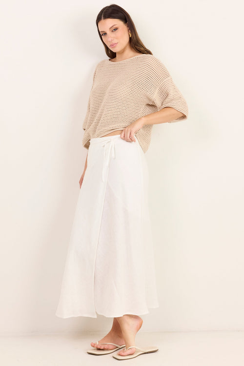 A woman modeling a beige knit short-sleeve top and white wide-leg skirt against a plain off-white studio background.