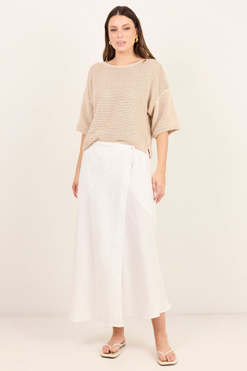 A woman modeling a beige knit short-sleeve top and white wide-leg midi skirt against a plain off-white studio background.