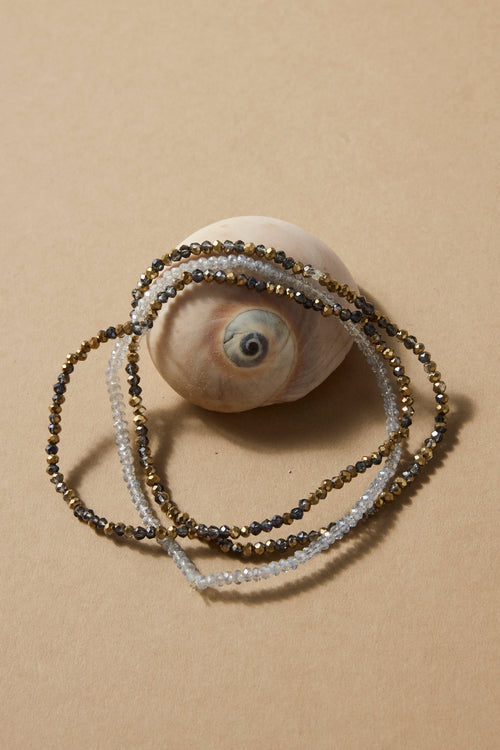 Three beaded bracelets on a shell with a beige background