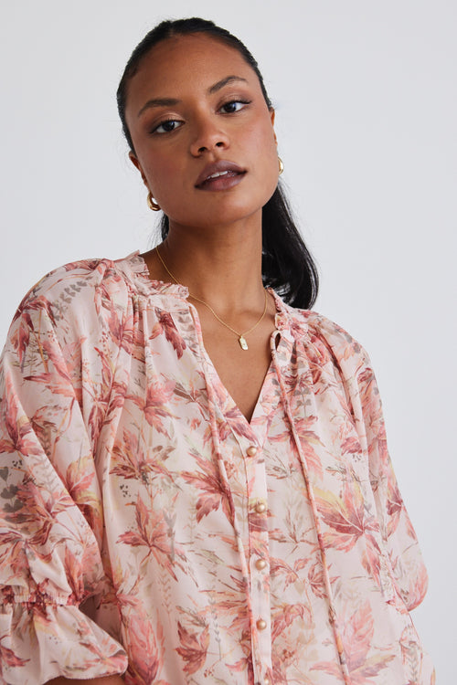 Model wears a floral blouse with white linen pants.