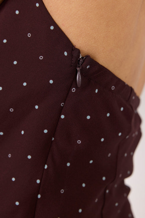 Close-up of a dark brown or very deep burgundy fabric with a small white polka dot pattern, showing a zipper detail and part of a model's skin.