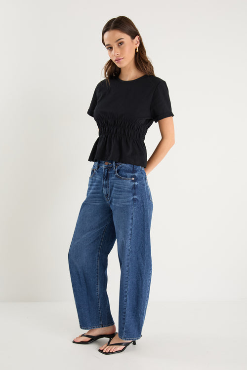 Woman wearing a black top and blue jeans on a white background