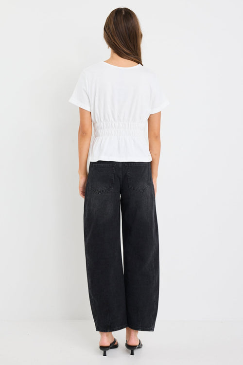 Woman wearing an ivory short sleeve cotton tee with shirred waist detail and a subtle peplum hem, styled with black jeans.
