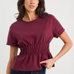 Woman wearing a maroon top and dark jeans on a white background