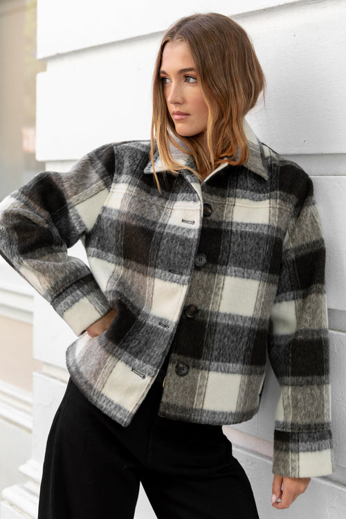 Woman wearing a plaid jacket against a white wall