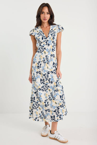 Woman wearing a floral dress with white sneakers on a plain background