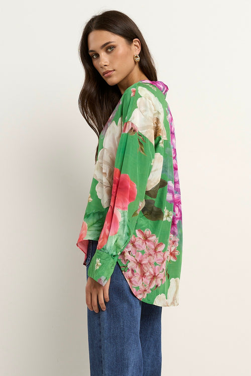 Woman wearing a green oversized button-up shirt with large floral print in pink, white, and beige tones.