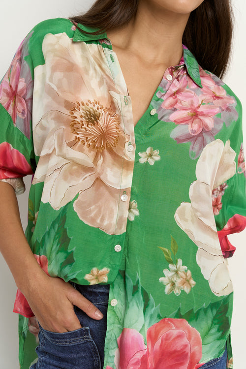 Woman wearing a green oversized button-up shirt with large floral print in pink, white, and beige tones.