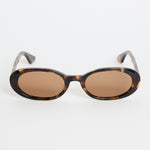 Narrow tortoiseshell oval sunglasses with warm brown tinted lenses, photographed against a white background
