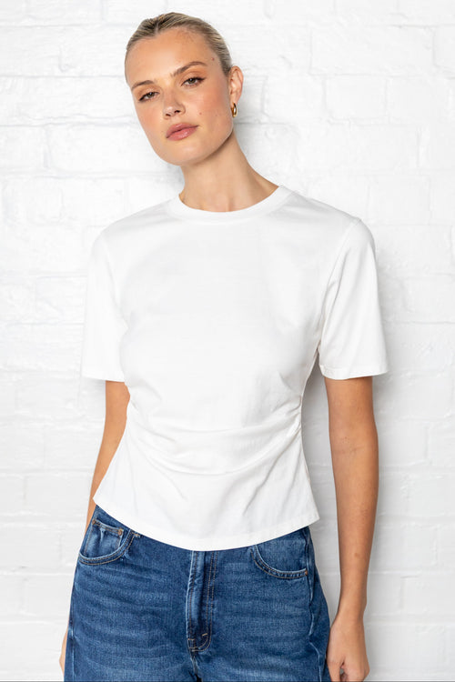 Woman wearing a white t-shirt with side ruching and blue jeans against a plain background