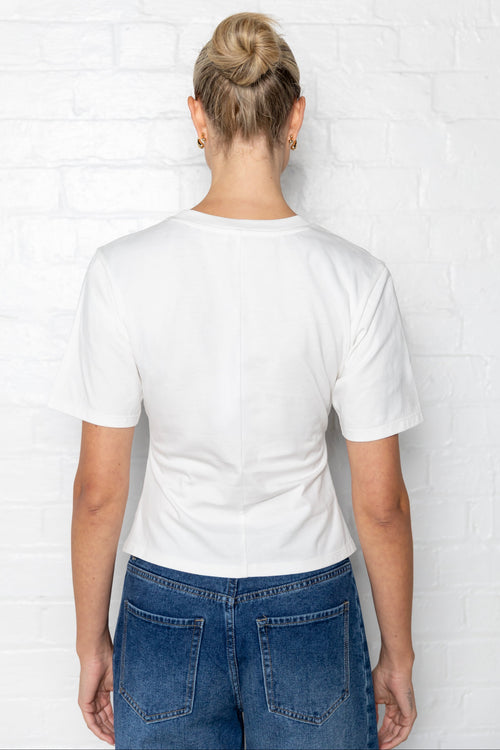 Woman wearing a white t-shirt with side ruching and blue jeans against a plain background