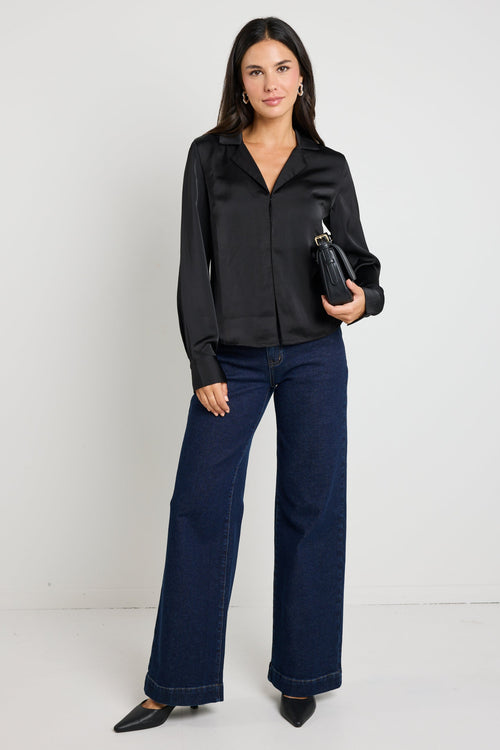 Woman wearing a black satin button-down shirt with a sleek silhouette, paired with dark jeans for a chic and sophisticated look.