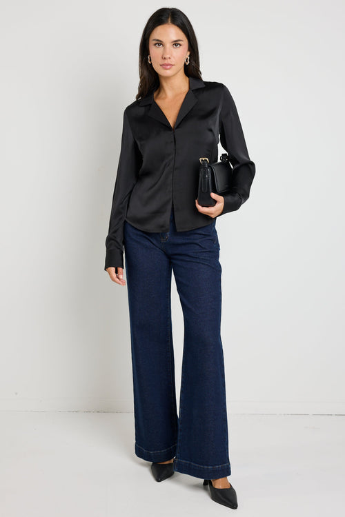 Woman wearing a black satin button-down shirt with a sleek silhouette, paired with dark jeans for a chic and sophisticated look.