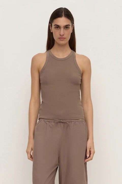 A woman modeling a sleeveless ribbed tank top and matching drawstring pants in a taupe-brown color, set against a plain off-white studio background.