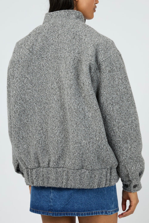 Model wears a grey marle bomber jacket with a textured wool-blend finish. The jacket features a high collar, front zip closure, and relaxed fit with side pockets. Layered over a striped button-down shirt and styled with a denim mini skirt for a casual yet elevated outfit.