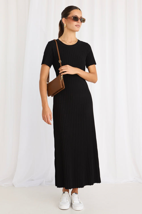 model wears a black knit midi dress and white sneakers and a brown handbag