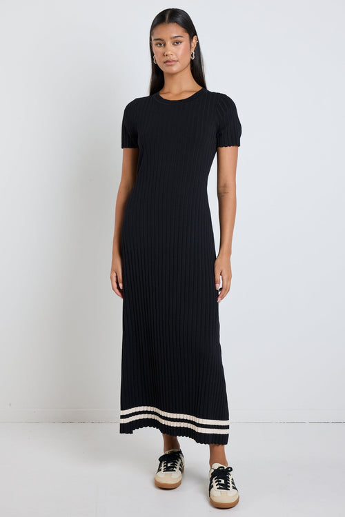 Woman wearing a black rib knit midi dress with short sleeves, styled with white sneakers for a chic and casual look.