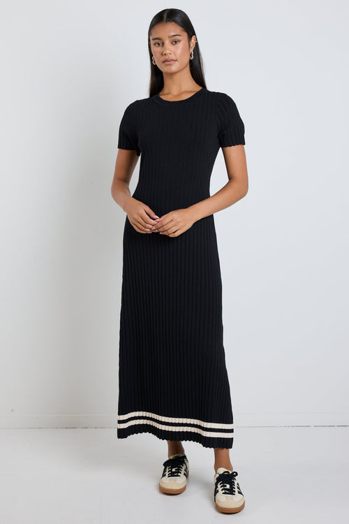 Woman wearing a black rib knit midi dress with short sleeves, styled with white sneakers for a chic and casual look.