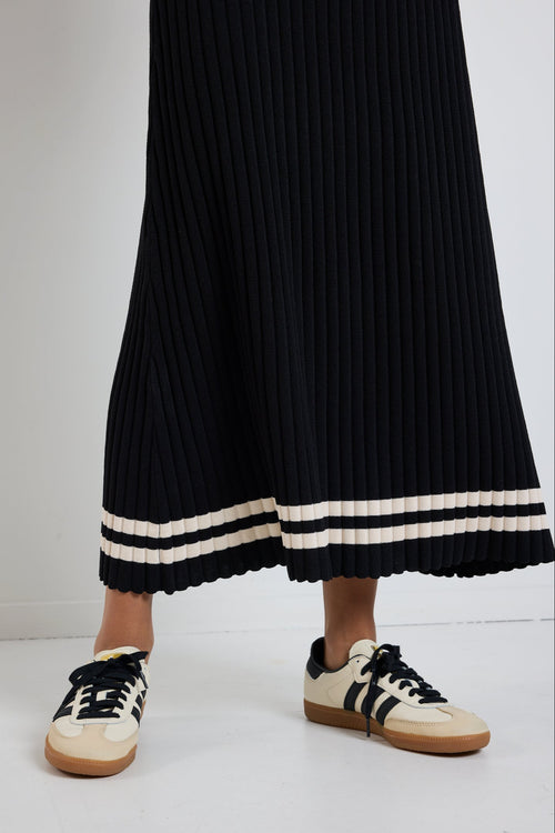 Woman wearing a black rib knit midi dress with short sleeves, styled with white sneakers for a chic and casual look.