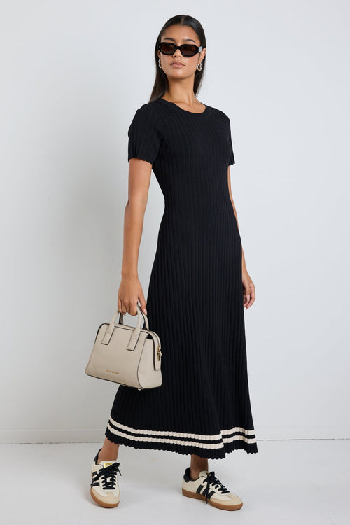 Woman wearing a black rib knit midi dress with short sleeves, styled with white sneakers for a chic and casual look.