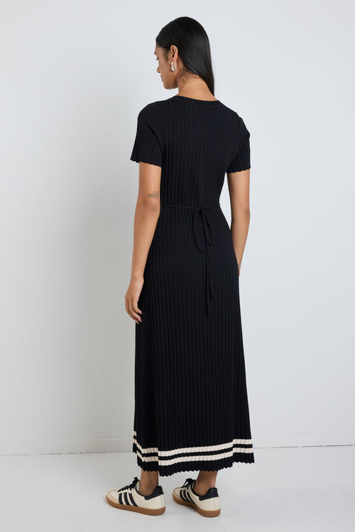 Woman wearing a black rib knit midi dress with short sleeves, styled with white sneakers for a chic and casual look.