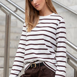 Woman wearing a black and white striped sweater and brown pants standing on a staircase.