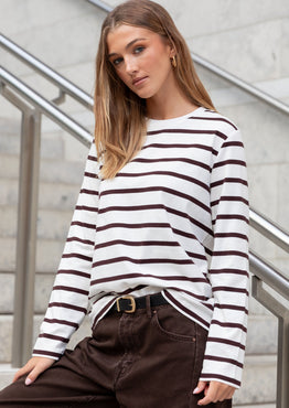 Woman wearing a black and white striped sweater and brown pants standing on a staircase.