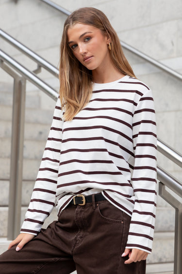 Woman wearing a black and white striped sweater and brown pants standing on a staircase.