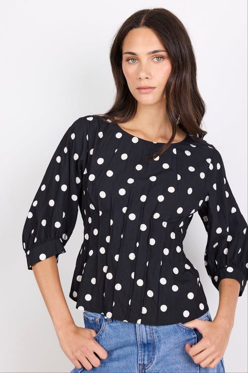Woman wearing a black blouse with white polka dots and blue jeans on a white background