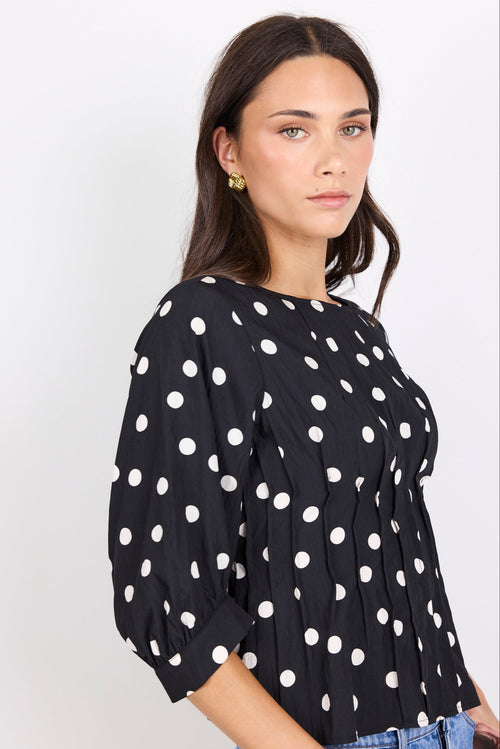 Woman wearing a black blouse with white polka dots against a white background