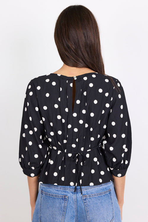 Woman wearing a black polka dot blouse with blue jeans on a white background