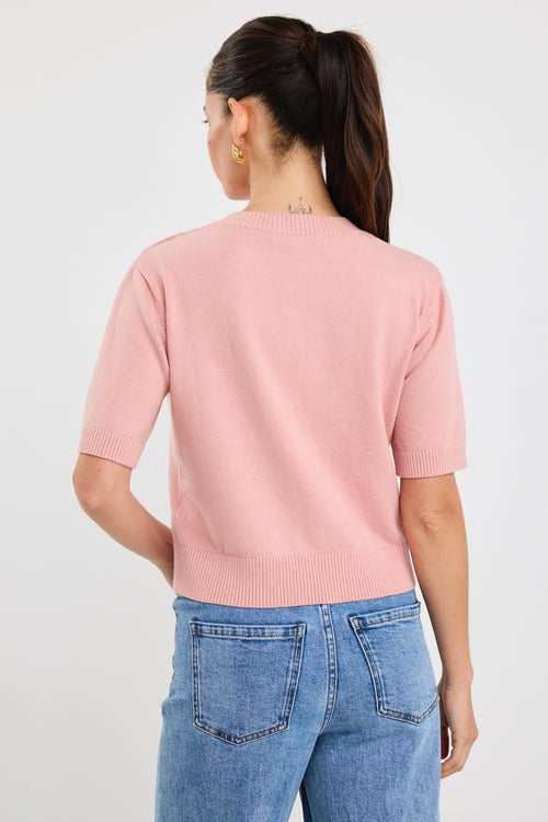 Woman wearing a blush pink short sleeve knit top with crew neckline and light blue high-waisted jeans.