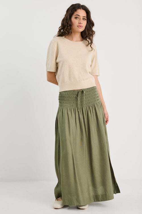 Woman wearing a beige top and green skirt on a white background
