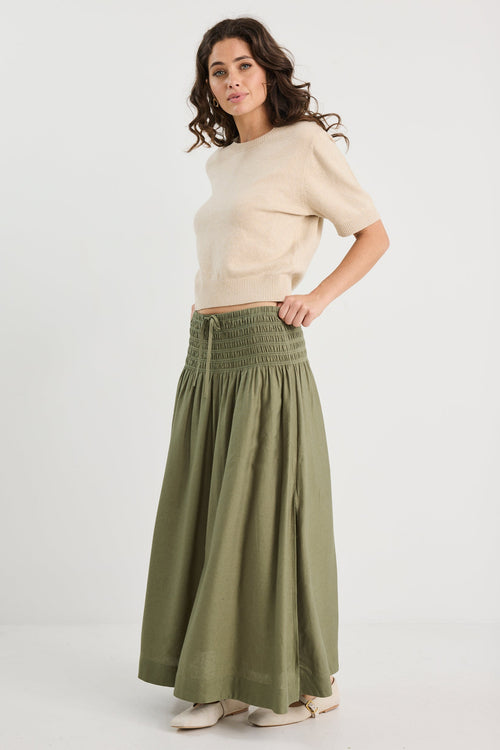 Woman wearing a beige sweater and green skirt on a white background