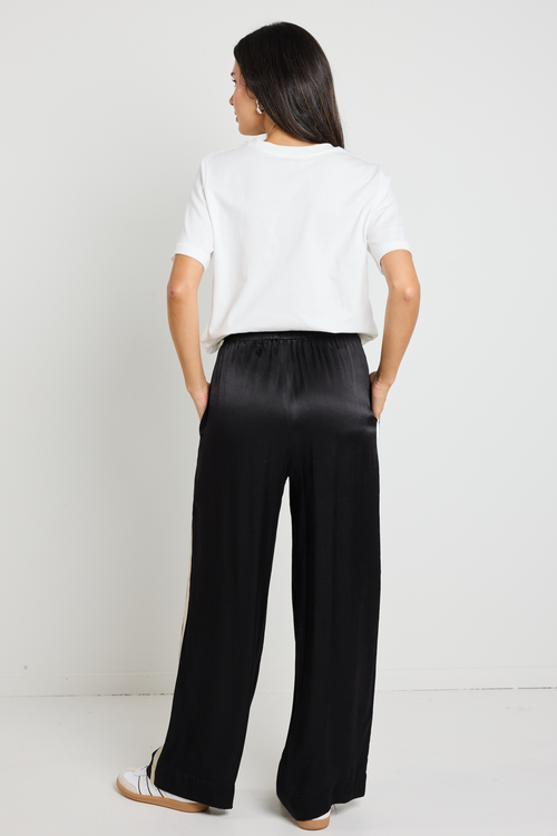 Woman wearing black Townie satin pants with a sandy beige side stripe, paired with a white tee for a sporty yet sophisticated look.