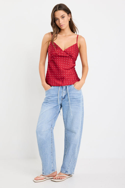 Woman wearing a red satin cami with white polka dots, bias-cut fit, and thin straps, styled with light blue jeans.