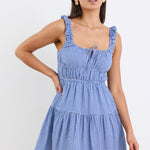A sleeveless electric blue and white gingham mini dress with tiered detailing, tie-front feature, and a flattering fit. Fully lined for comfort, made from a 50% Cotton and 50% Viscose blend.
