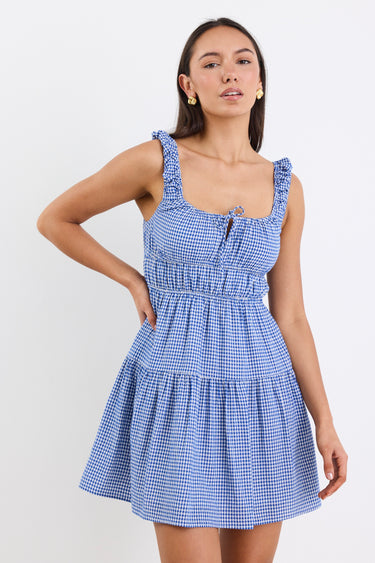 A sleeveless electric blue and white gingham mini dress with tiered detailing, tie-front feature, and a flattering fit. Fully lined for comfort, made from a 50% Cotton and 50% Viscose blend.