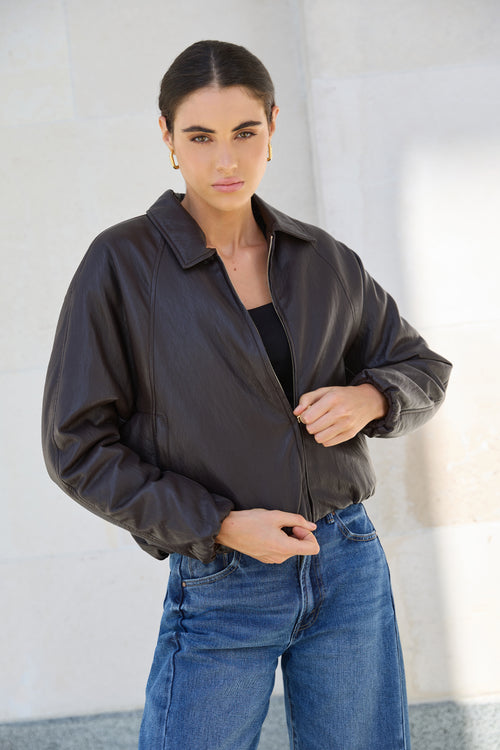 Woman wearing a black jacket and blue jeans against a light background