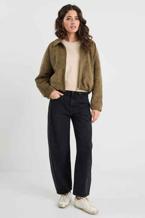 Woman wearing a khaki mock suede zip-up jacket with a soft, textured finish and a relaxed fit, styled over a beige knit top and black jeans.