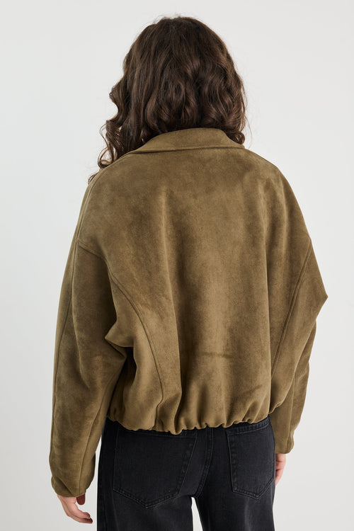 Woman wearing a khaki mock suede zip-up jacket with a soft, textured finish and a relaxed fit, styled over a beige knit top and black jeans.