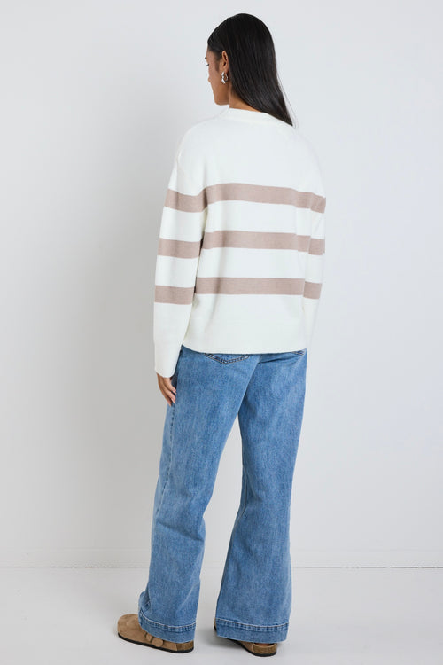 A cosy natural and taupe striped crewneck sweater styled with blue denim, creating a relaxed yet refined everyday look.
