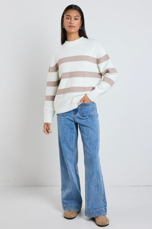 A cosy natural and taupe striped crewneck sweater styled with blue denim, creating a relaxed yet refined everyday look.
