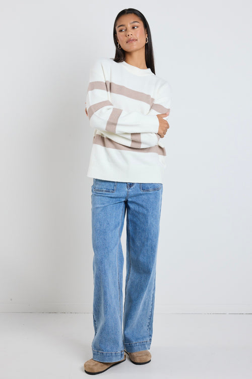 A cosy natural and taupe striped crewneck sweater styled with blue denim, creating a relaxed yet refined everyday look.