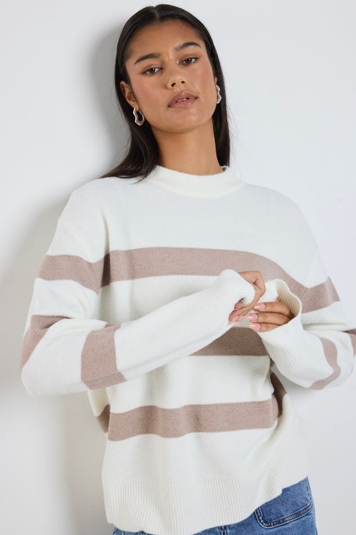 A cosy natural and taupe striped crewneck sweater styled with blue denim, creating a relaxed yet refined everyday look.