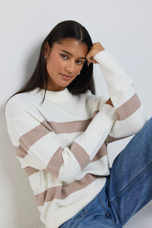A cosy natural and taupe striped crewneck sweater styled with blue denim, creating a relaxed yet refined everyday look.